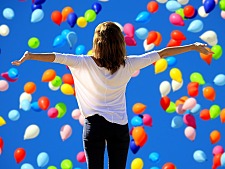 Frau vor dem Hintergrund eines Himmels voller Luftballons, die Arme ausgebreitet